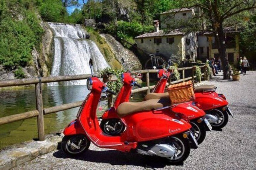 Two red scooters parked near a waterfall. 2