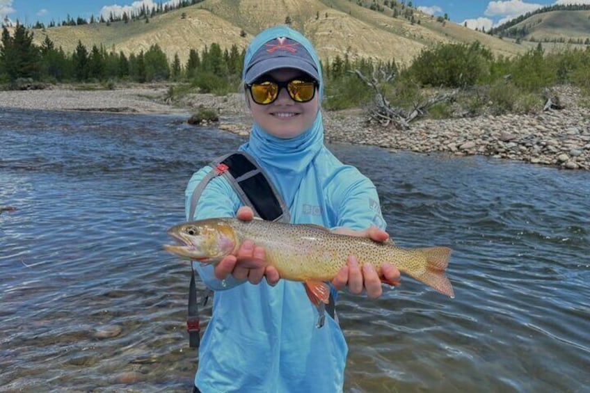Una persona tiene un pesce in un fiume, con montagne sullo sfondo. 3