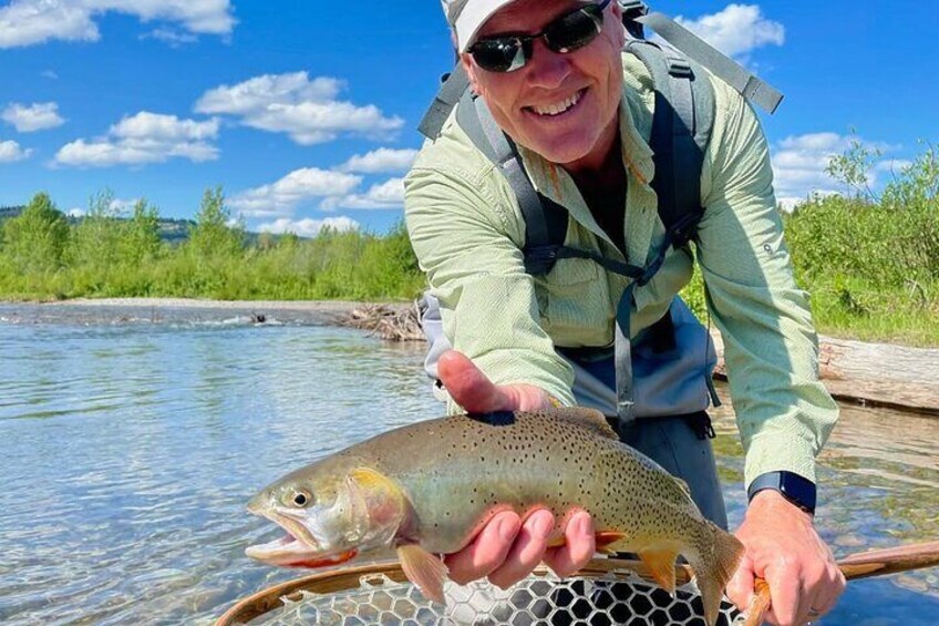 Una persona tiene un pesce in un ruscello cristallino, sullo sfondo c'è del verde. 4