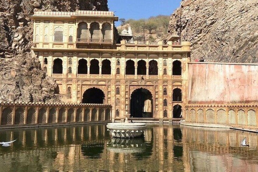 Un edificio storico con architettura elaborata, un grande ingresso ad arco e una superficie d'acqua specchiante davanti. 2