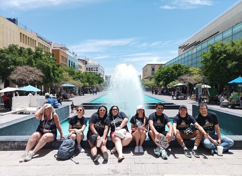 A group of people sitting by a fountain in an urban plaza with buildings and trees around. 4