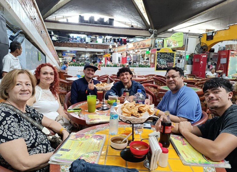 A group of people dining at an outdoor restaurant with a tiled floor and various food items on the table. 3