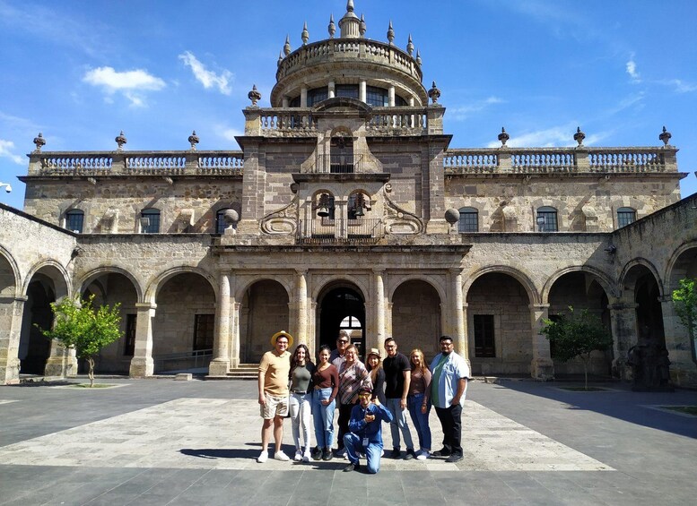 A historic building with a central dome, arched colonnades, and a group of people posing in front. 4