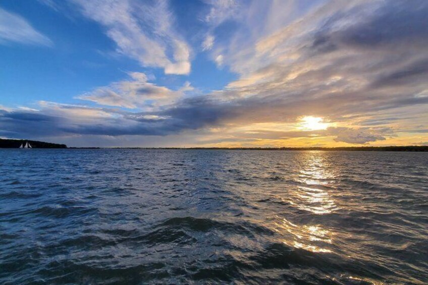 A sunset over a body of water with a sailboat and a distant shoreline. 2