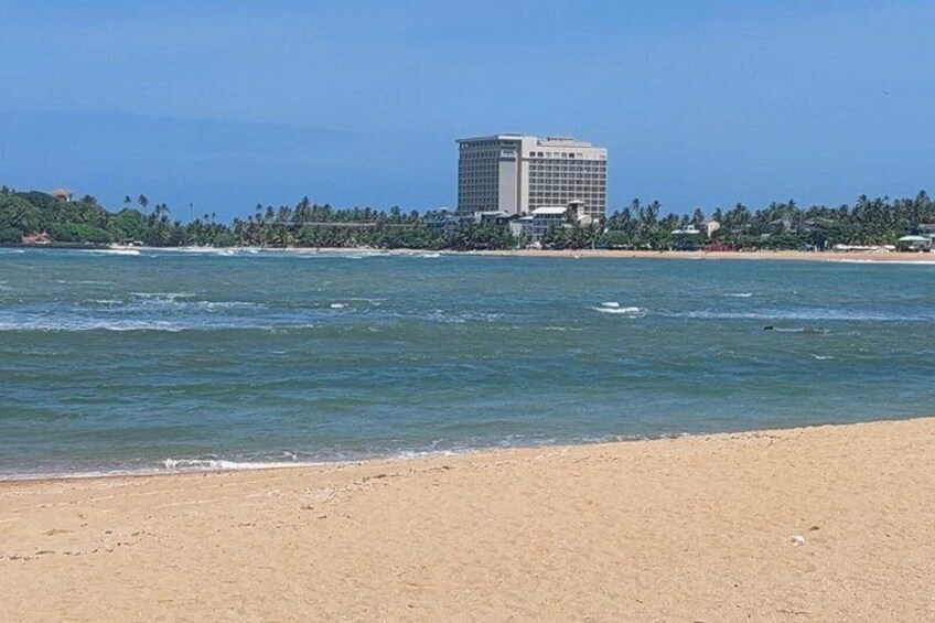 Una playa con agua cristalina, una orilla arenosa y un edificio alto al fondo. 4