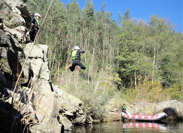 A person jumping off a cliff into a river, with a boat and forest in the background. 5