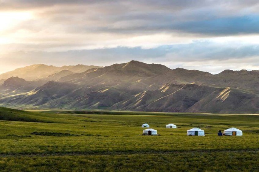 A grassy field with yurts and mountains in the background. 2