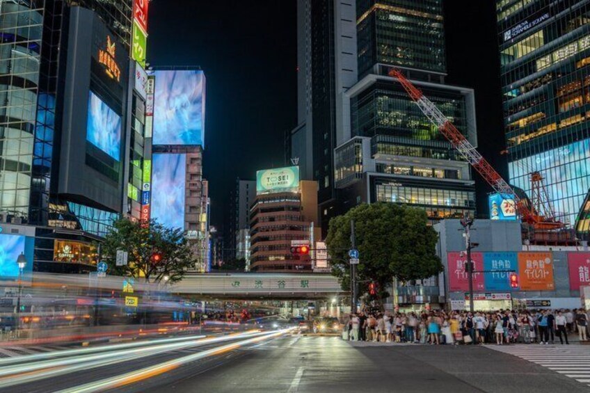 Une vue nocturne d’une ville, avec des panneaux publicitaires illuminés, une rue animée et une foule de personnes. 4