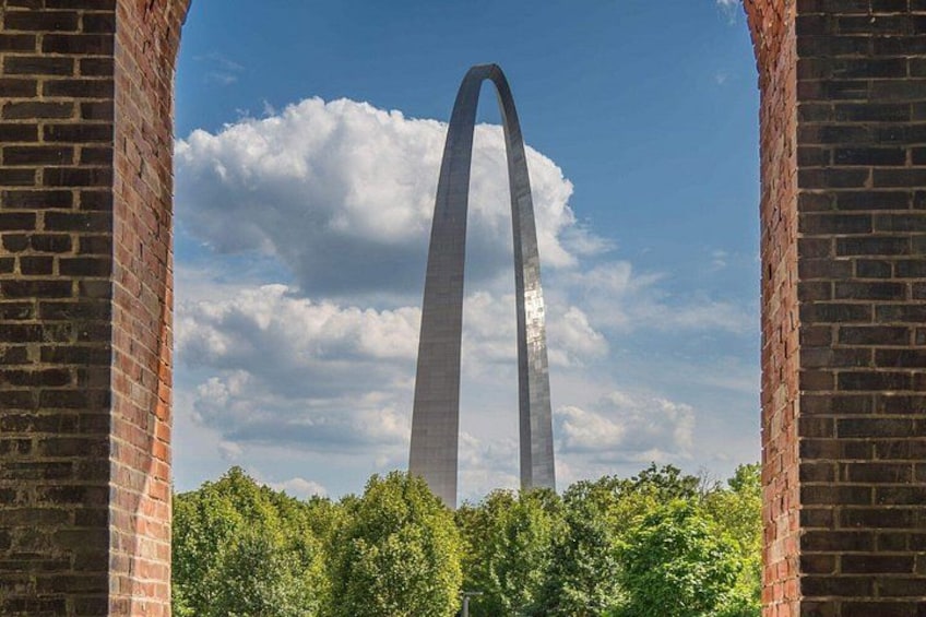 A tall, narrow monument framed by brick arches, with a clear sky and clouds in the background. 3