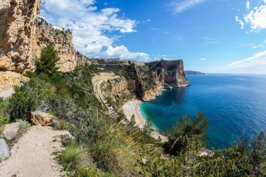 A coastal cliff with a winding path, a beach, and a clear blue sea. 4