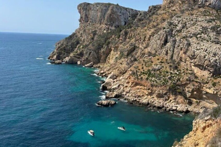 A coastal cliff with clear turquoise waters, rocky terrain, and a small boat anchored near the shore. 5