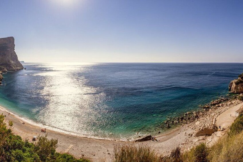 A coastal landscape with a beach, clear blue sea, and a cliff. 2