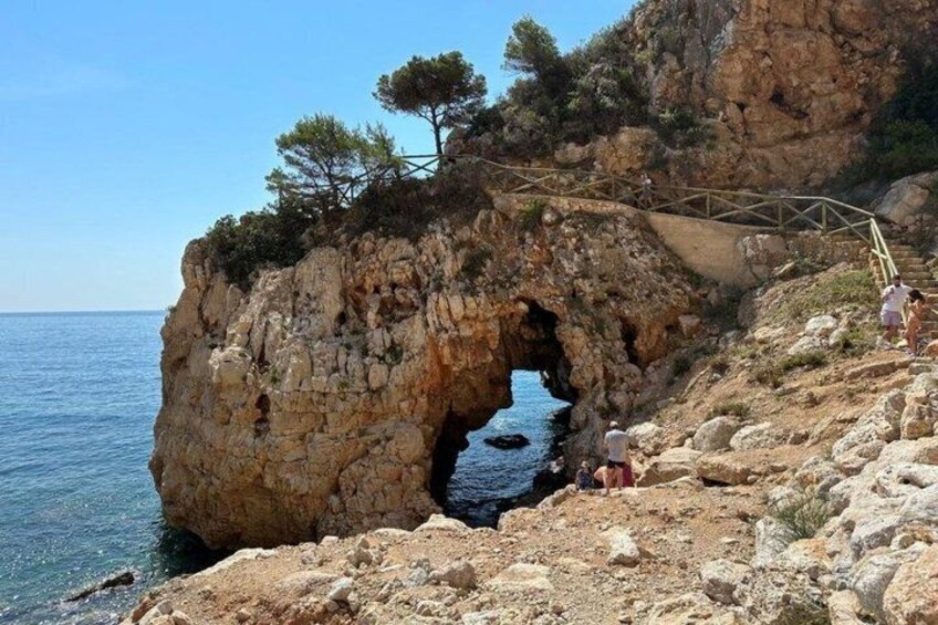 A rocky coastline with a natural arch formation and a wooden bridge. 3