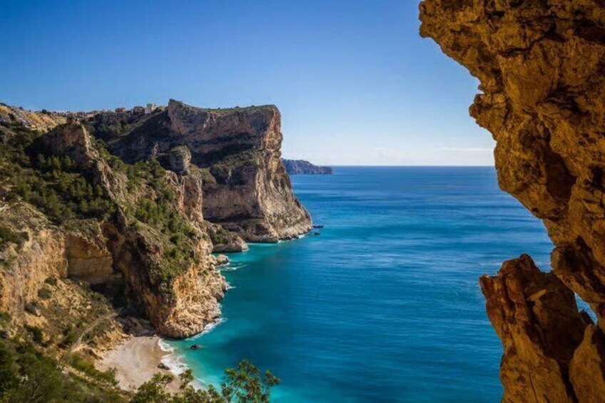 A coastal cliff with a beach and clear blue sea. 1