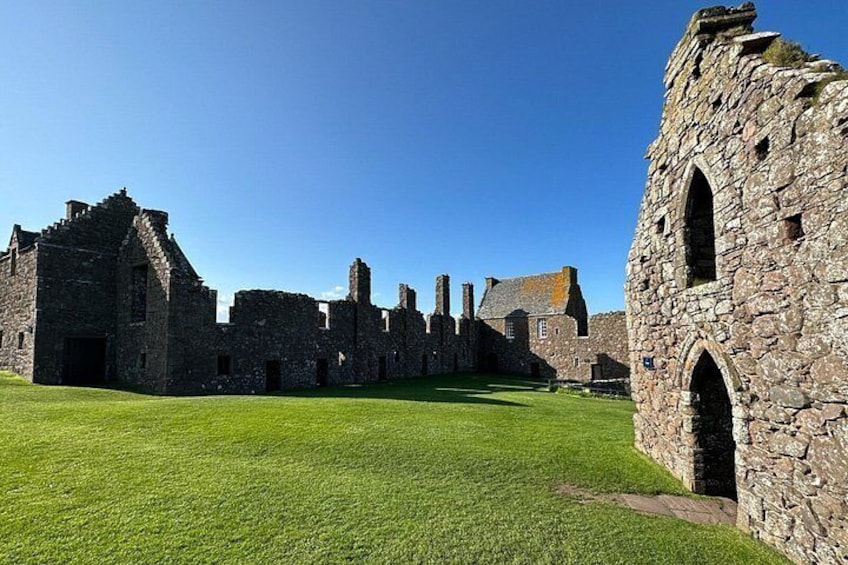 A historic stone building with ruins and a well-maintained lawn. 5
