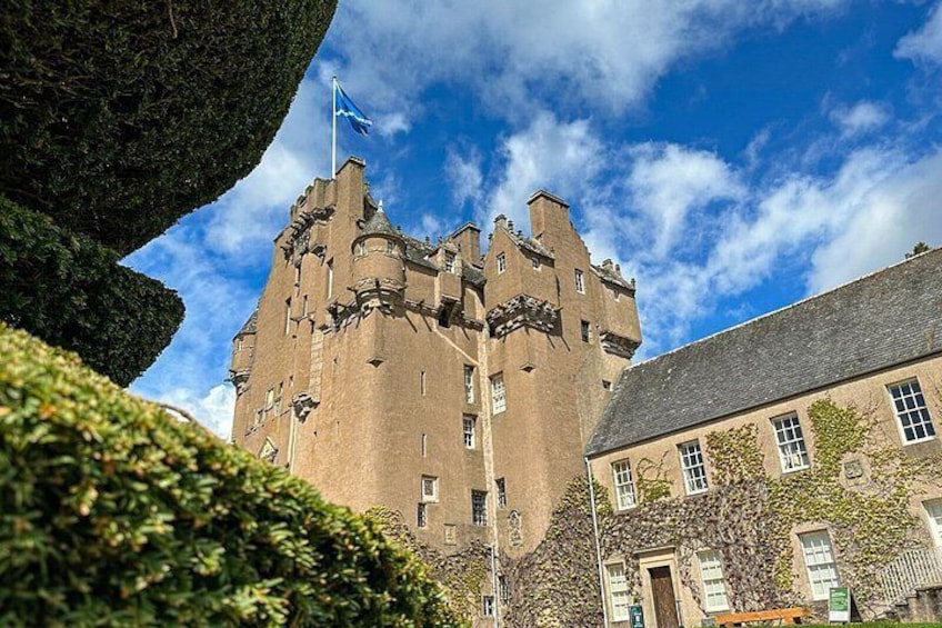 A castle with a flag, surrounded by greenery and a building with ivy. 1