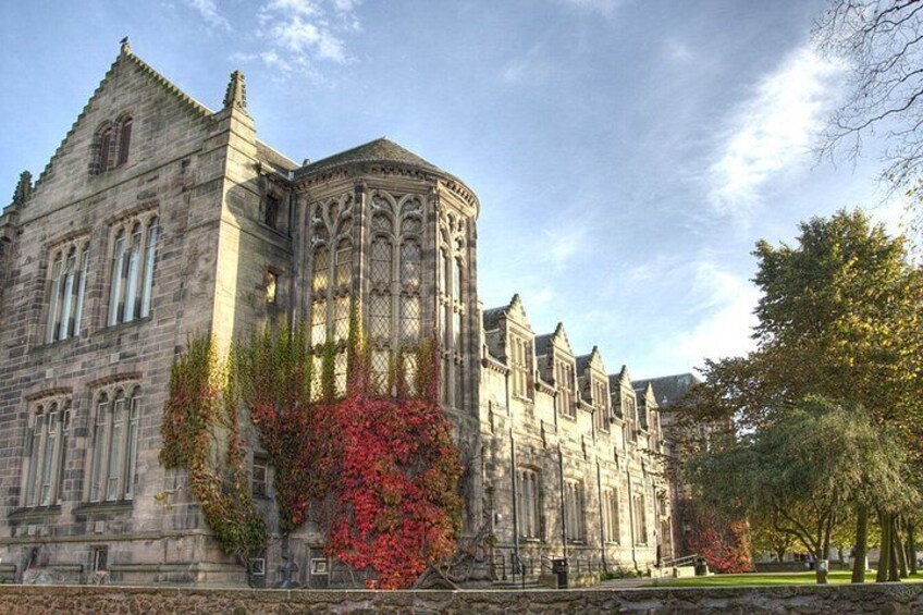 A historic stone building with a turret and arched windows, surrounded by trees with autumn foliage. 3