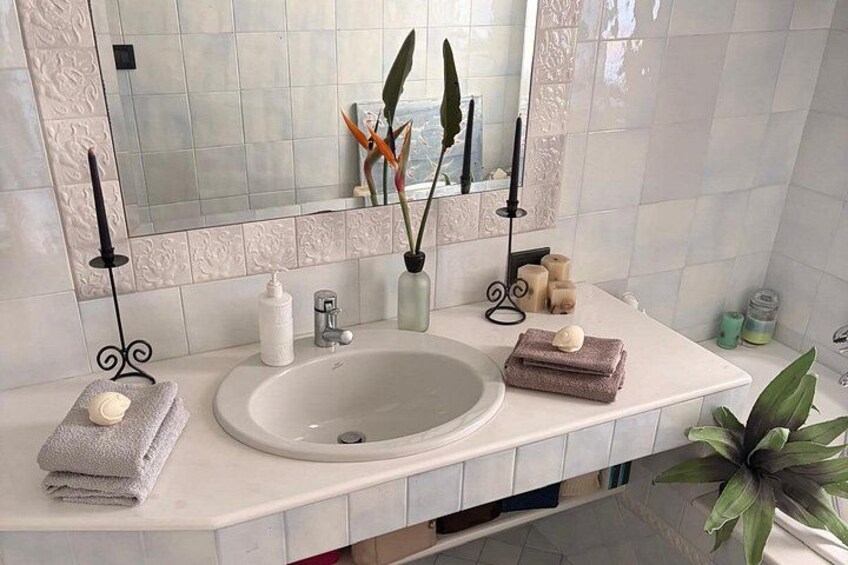 A bathroom with a white sink, mirror, and decorative items including candles, a plant, and toiletries. 2