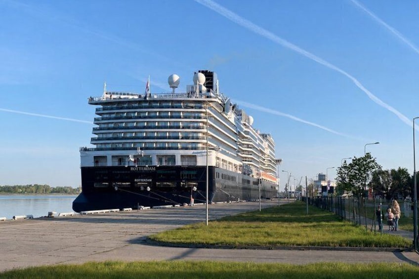 A large cruise ship named 'Rotterdam' docked at a port with a clear sky and calm water in the background. 5