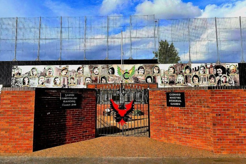 A brick wall with a gate, a mural of people, and a sign for Clonard Martyrs Memorial Garden. 3