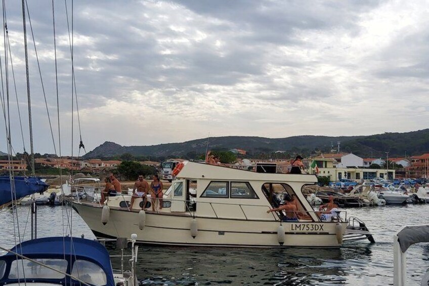 Un barco amarrado en un puerto deportivo, con gente a bordo, rodeado de otros barcos y edificios al fondo. 2