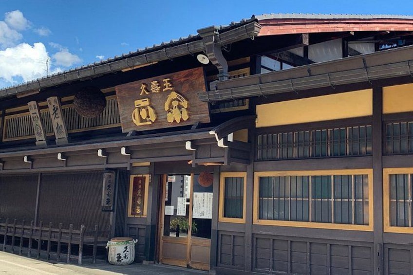 Un edificio tradicional japonés con un letrero, ventanas de celosía de madera y techo de tejas. 5