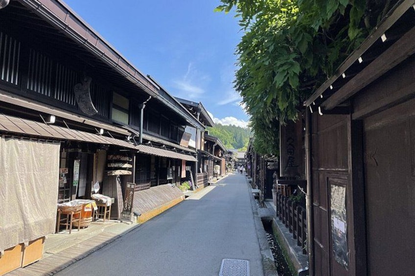 Una calle estrecha bordeada de edificios tradicionales de madera, un cielo despejado y una cordillera distante. 3