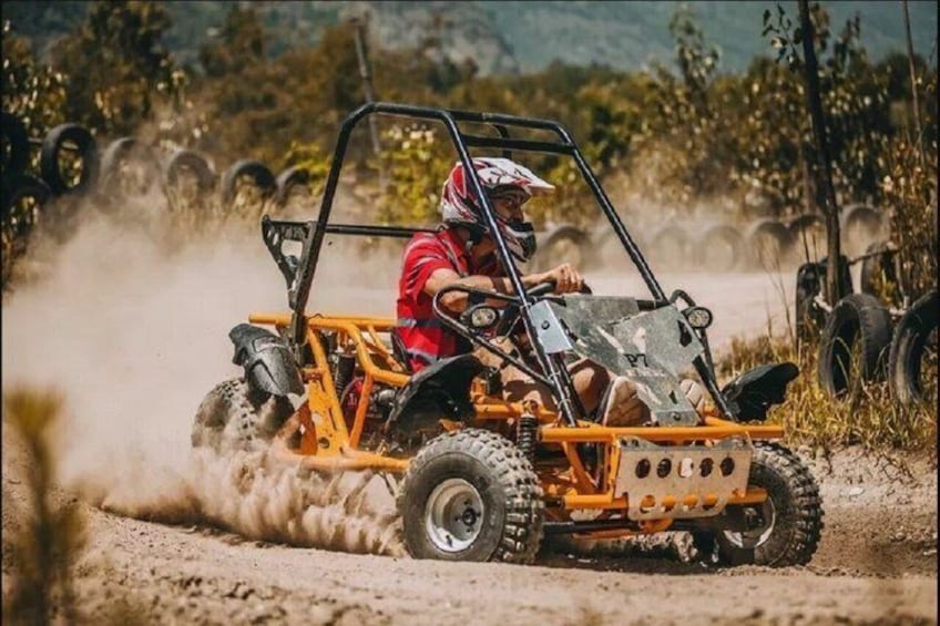 A person driving a yellow off-road vehicle on a dirt track with tires kicking up dust. 1