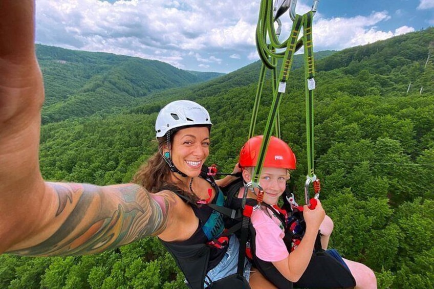 Two people on a zipline with a forested mountain landscape in the background. 3