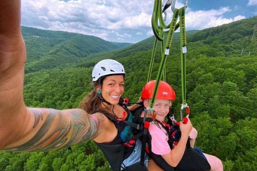 Two people on a zipline with a forested mountain backdrop. 3