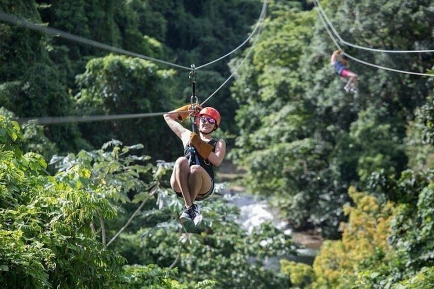 A person zip-lining through a forested area with dense greenery and a river in the background. 3
