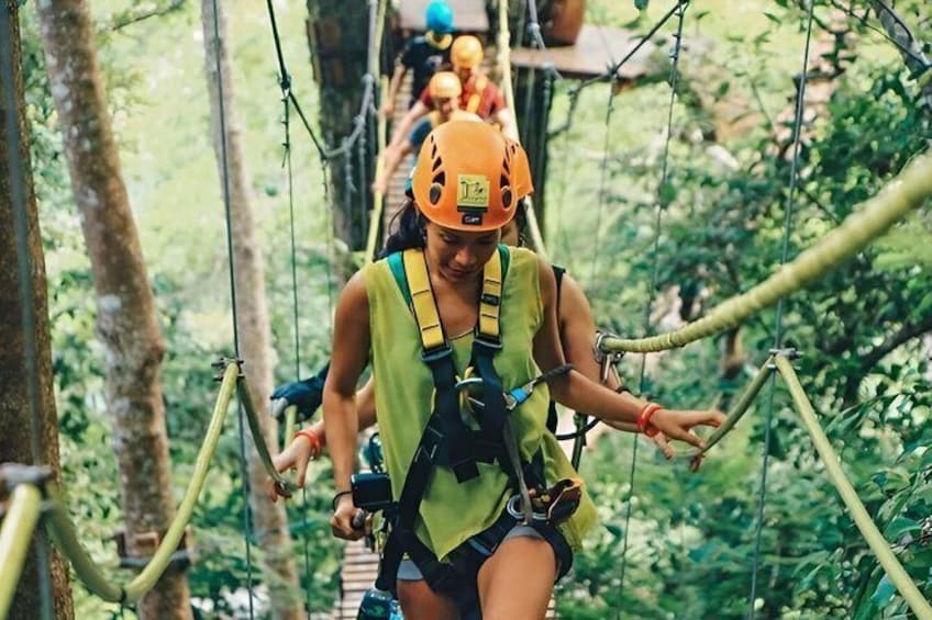 An individual navigating a rope bridge in a forested area. 2