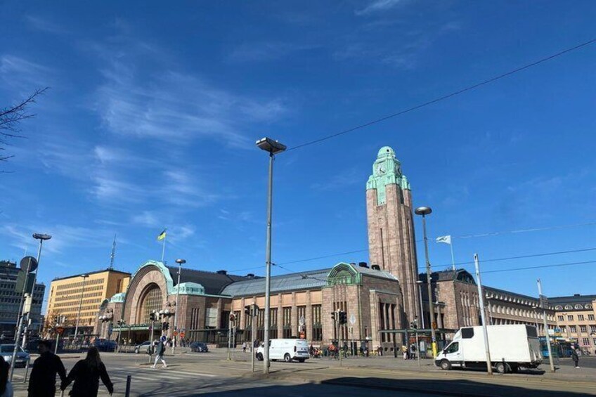A large building with a clock tower, a tram, and a white van on the street. 3