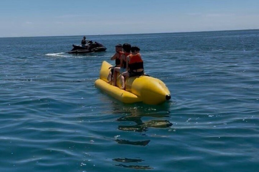 En gul flotte med två personer ombord, ute på havet, med en vattenskoter i bakgrunden. 2