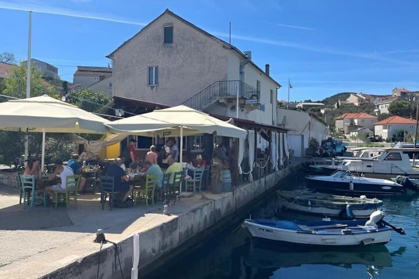 A marina with boats docked, people dining at outdoor tables, and a building in the background. 3
