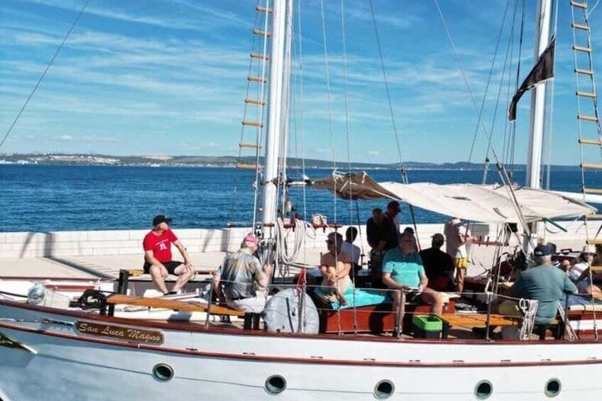 A sailboat with people on deck, a clear sky, and calm water. 2