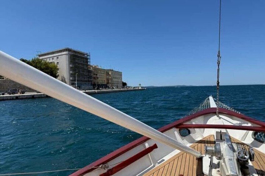 A boat's deck with a clear view of the water, a distant building, and a small boat in the background. 4