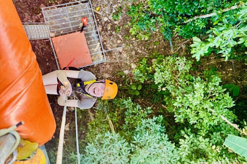 Eine Person mit Bungee-Ausrüstung, darunter Sicherheitsgurt und Helm, springt aus und wird von dichtem Grün umgeben. 2