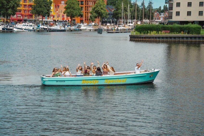 En båd med passagerer på en rolig flod, omgivet af bygninger og træer. 5