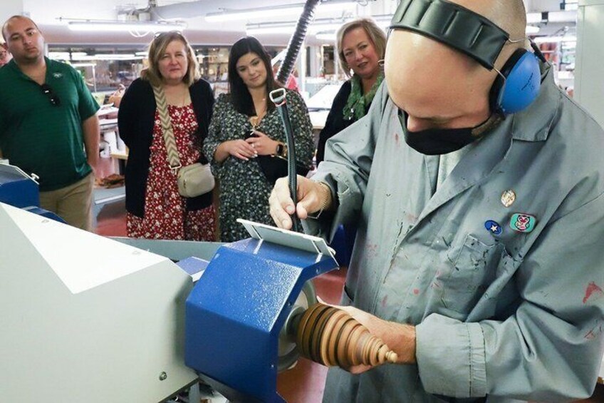 En person i en blå arbejdsuniform betjener en maskine med et blåt kontrolpanel, omgivet af tilskuere. 1