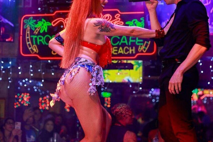 Una artista con top rojo y falda de red, con un letrero de neón al fondo. 3