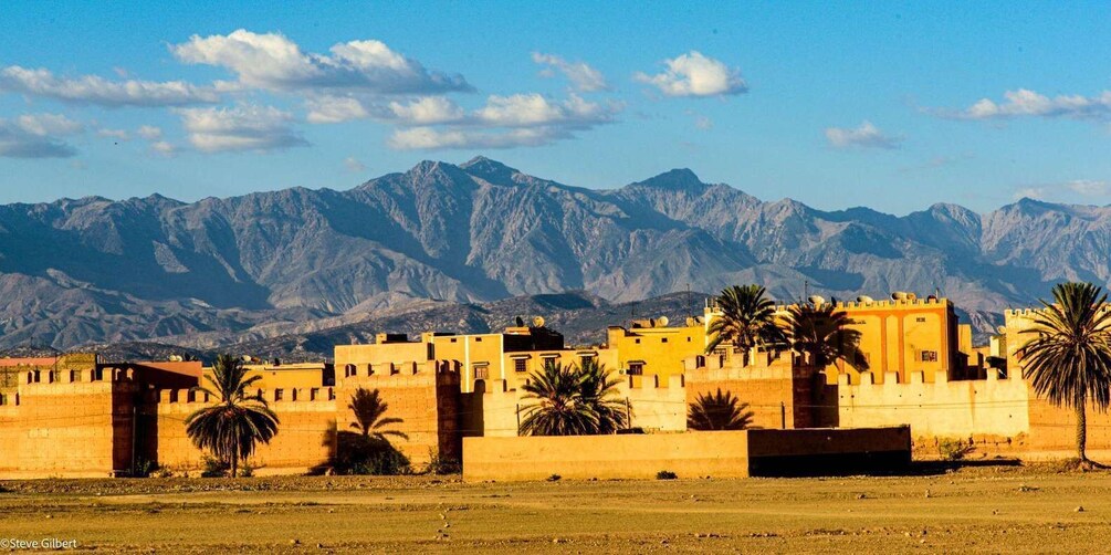 A fortified city with palm trees and mountains in the background. 2