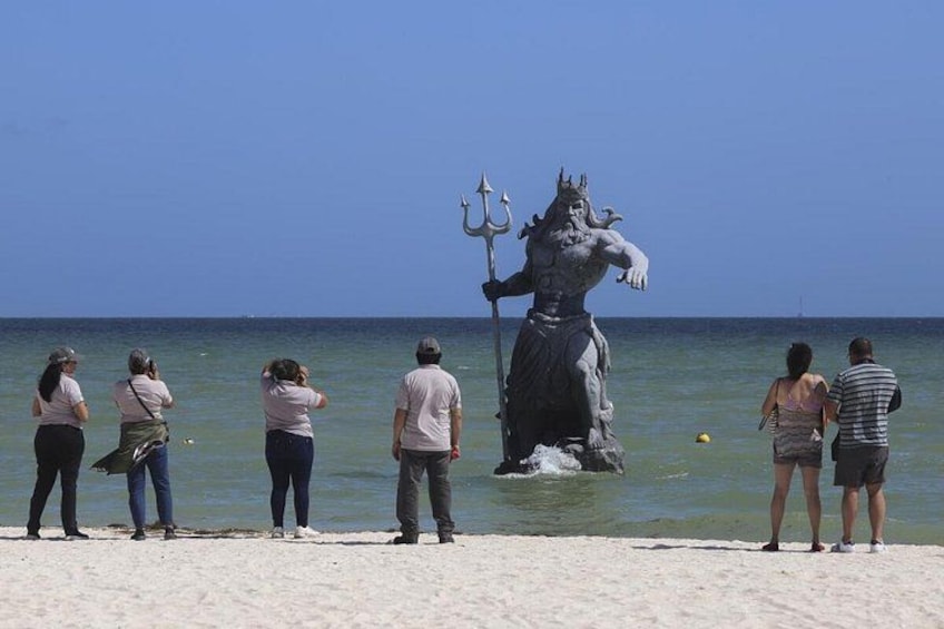 A statue of a mythological figure on a beach with people observing it. 5