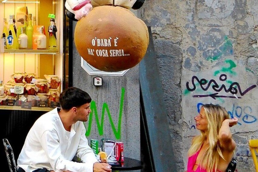 A man sitting at a table with a woman standing beside him, a large food dispenser, and a wall with graffiti. 4