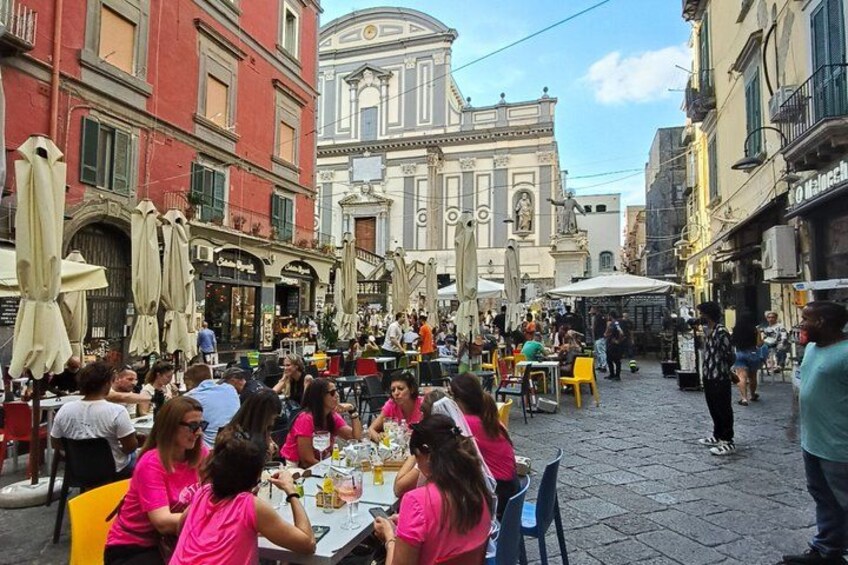 A bustling outdoor café with tables and chairs, surrounded by historic buildings and a prominent church dome. 3