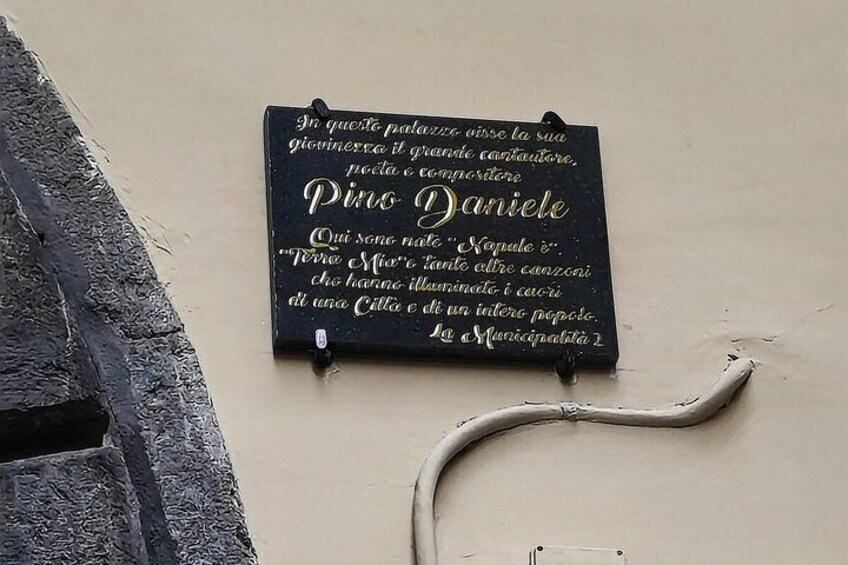 Ein schwarzes Schild mit weißer Schrift auf einer beigen Wand, an einer Steinwand befestigt. 3