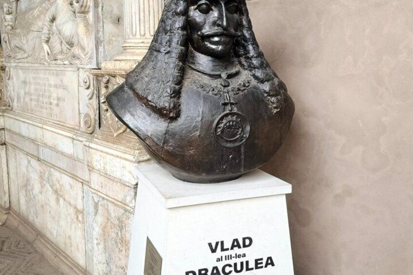 Eine Büstenstatue mit einer Plakette, auf der 'VLAD al III-lea alaculea' steht, auf einem Sockel. 4
