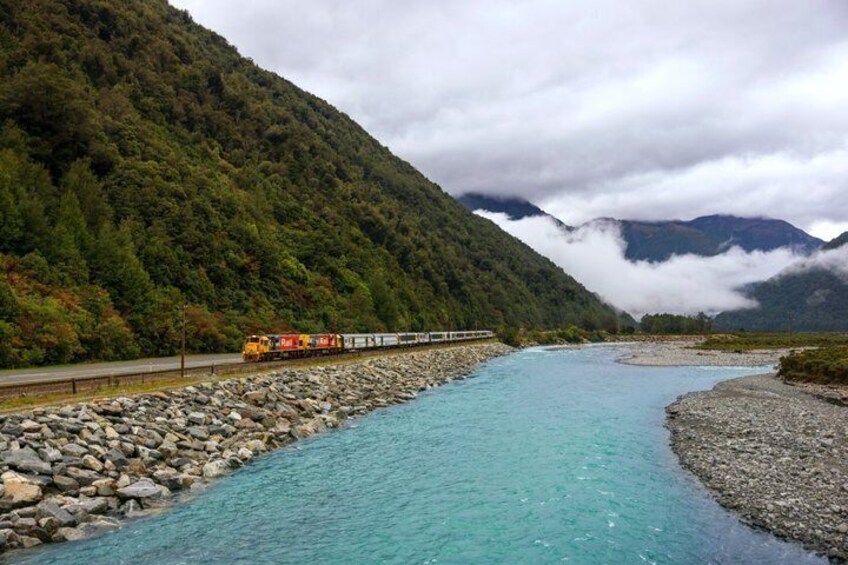 A train traveling along a river surrounded by mountains. 2