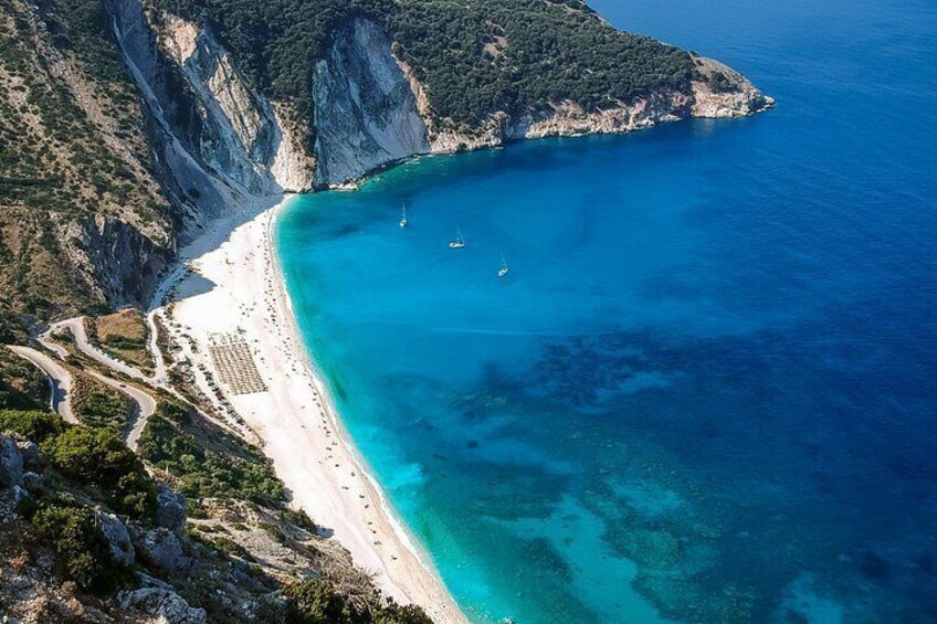 Paesaggio costiero con spiaggia, acque blu cristalline e scogliere rocciose. 2