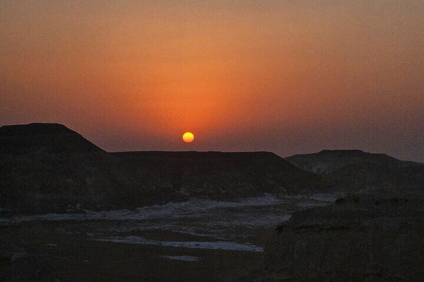 Un coucher de soleil sur un paysage désolé, avec des collines au premier plan. 5